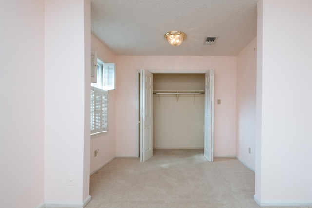 unfurnished bedroom with light colored carpet, a textured ceiling, and a closet