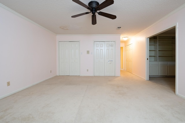 unfurnished bedroom with light carpet, a textured ceiling, ceiling fan, and multiple closets