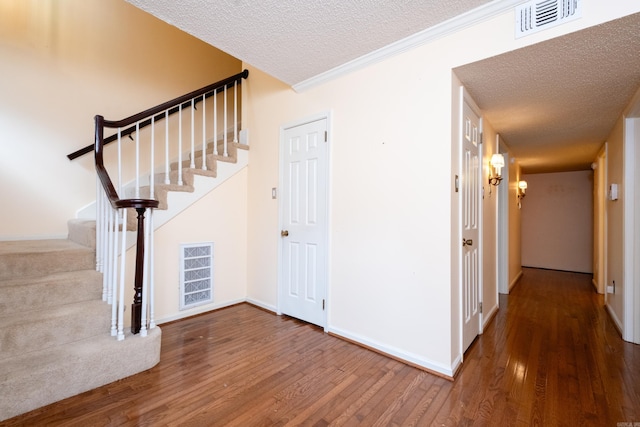 interior space with wood-type flooring, a textured ceiling, and ornamental molding