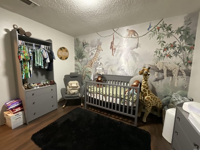 bedroom with dark hardwood / wood-style flooring, a nursery area, and a textured ceiling