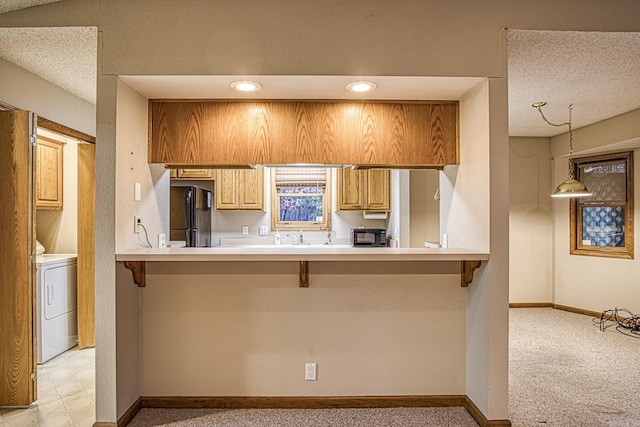 kitchen featuring black refrigerator, washer / dryer, kitchen peninsula, and a breakfast bar area