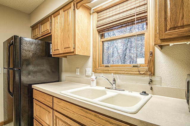 kitchen featuring black fridge, sink, and a textured ceiling