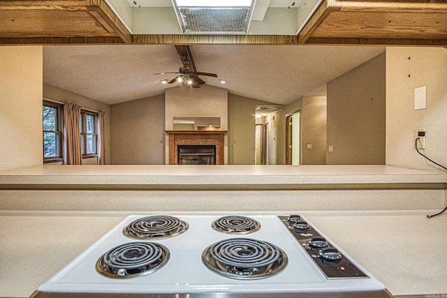 kitchen featuring lofted ceiling, ceiling fan, white gas stovetop, and a fireplace