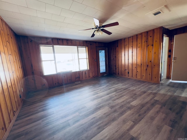 empty room featuring ceiling fan, dark hardwood / wood-style floors, and wooden walls