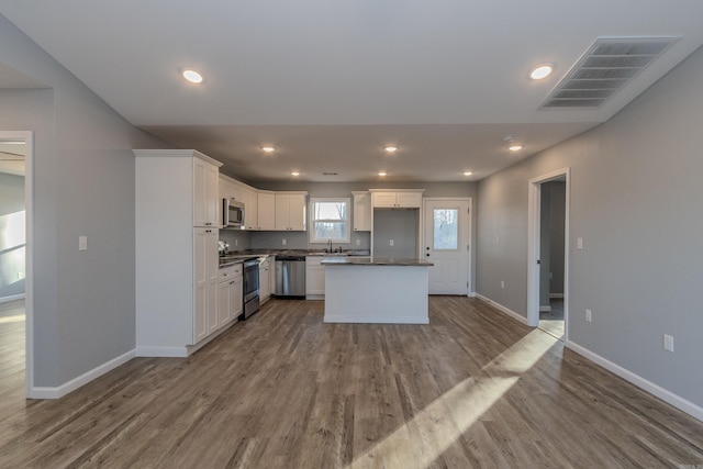 kitchen with sink, white cabinetry, a kitchen island, wood-type flooring, and stainless steel appliances