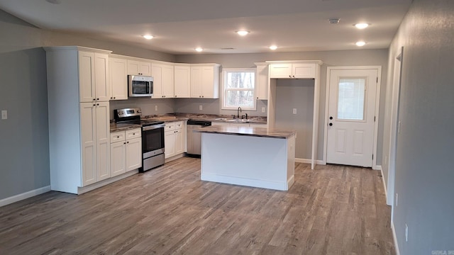 kitchen with a center island, white cabinets, sink, light wood-type flooring, and stainless steel appliances