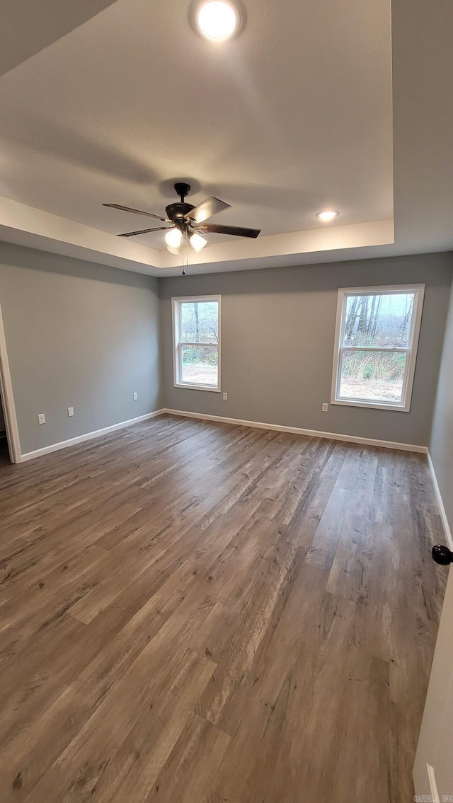 unfurnished room with a tray ceiling, ceiling fan, and dark hardwood / wood-style flooring