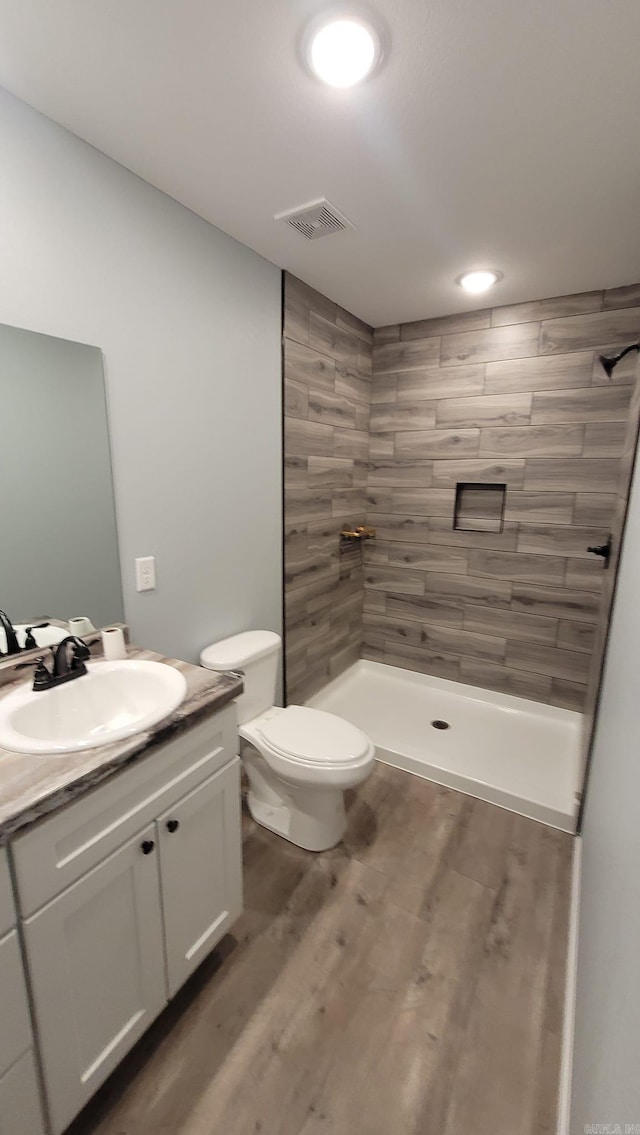 bathroom featuring tiled shower, hardwood / wood-style floors, vanity, and toilet