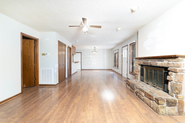 unfurnished living room with ceiling fan, a textured ceiling, hardwood / wood-style flooring, and a fireplace