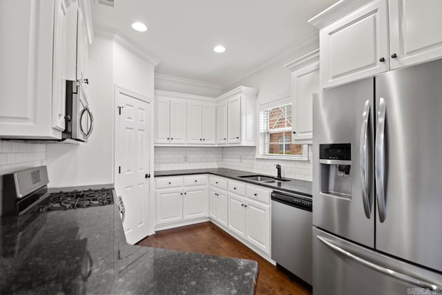 kitchen featuring sink, dark stone countertops, ornamental molding, appliances with stainless steel finishes, and white cabinetry