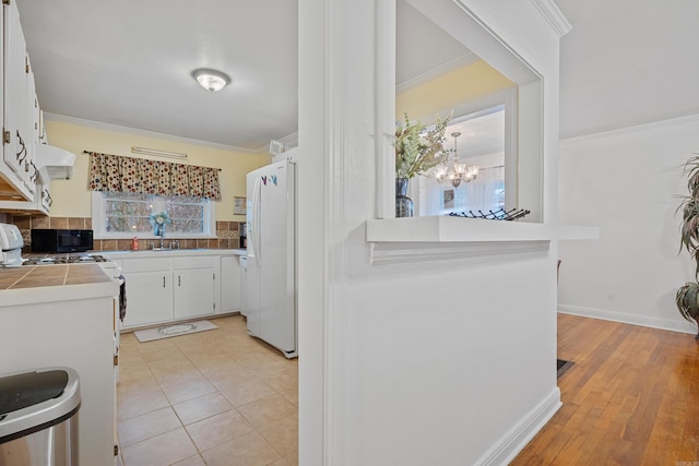 kitchen with an inviting chandelier, white cabinets, light wood-type flooring, tasteful backsplash, and white fridge