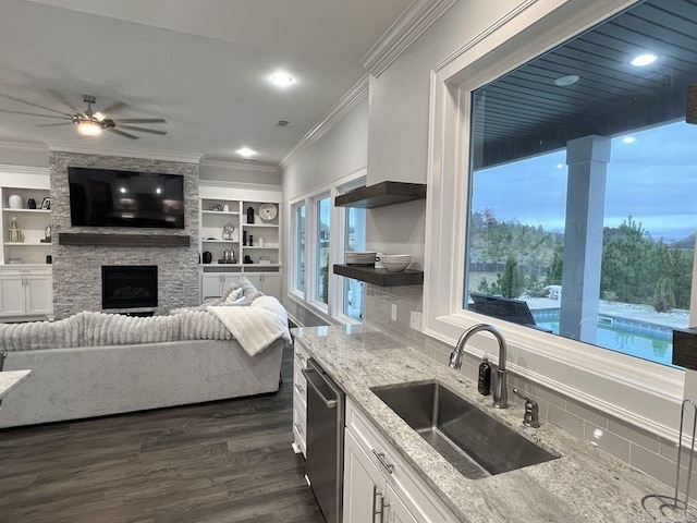 kitchen featuring white cabinetry, sink, dishwasher, a stone fireplace, and ornamental molding