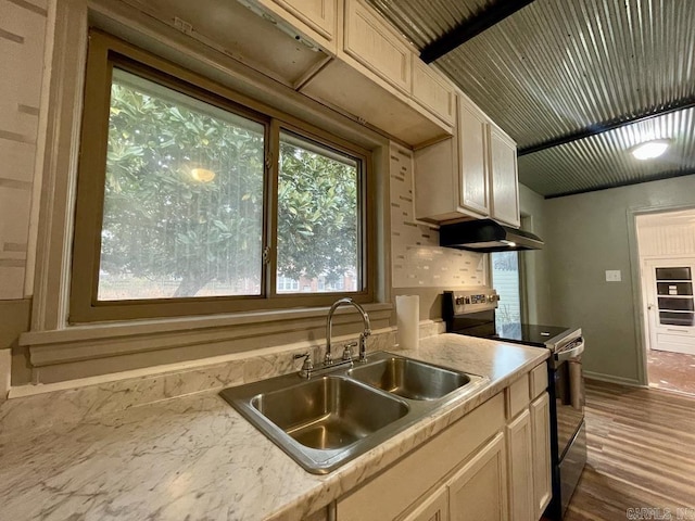 kitchen with a wealth of natural light, stainless steel electric range, light countertops, under cabinet range hood, and a sink