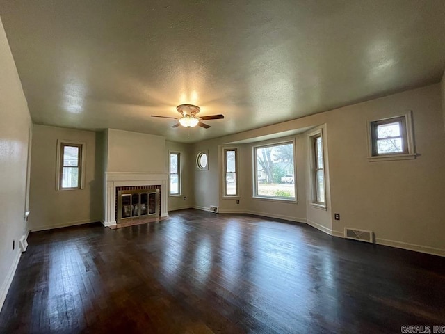 unfurnished living room featuring a fireplace with flush hearth, dark wood-style flooring, visible vents, and baseboards