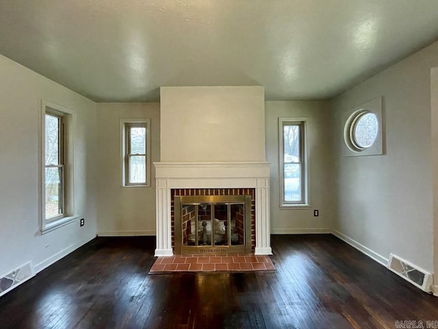 unfurnished living room featuring hardwood / wood-style flooring, a brick fireplace, and visible vents