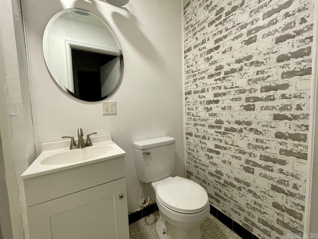 half bathroom featuring toilet, brick wall, tile patterned flooring, and vanity