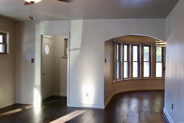 entryway featuring baseboards, arched walkways, ceiling fan, and dark wood-type flooring