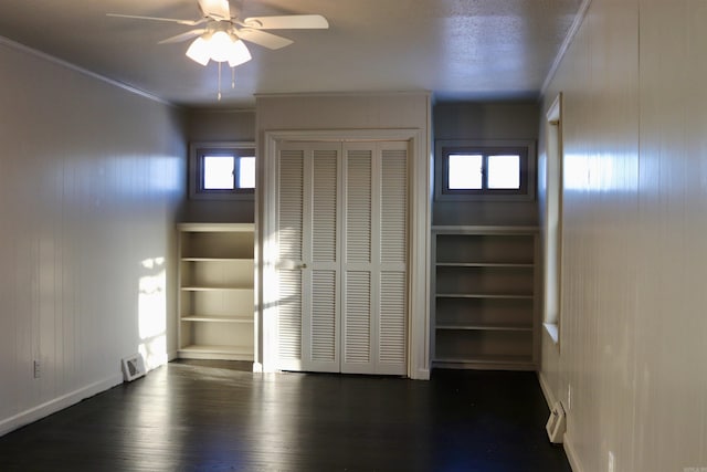 unfurnished bedroom with dark wood-style flooring, a closet, ornamental molding, a ceiling fan, and baseboards