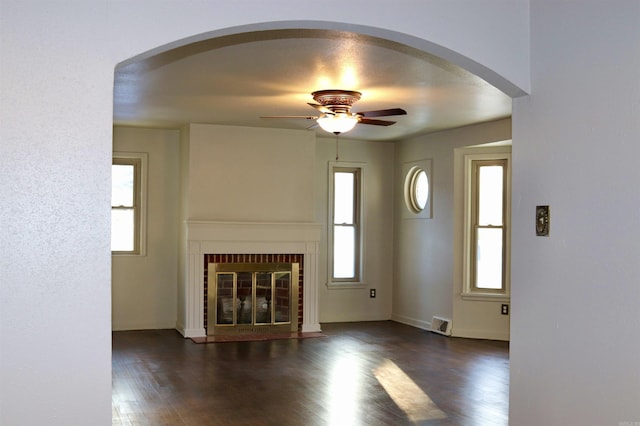 unfurnished living room featuring baseboards, visible vents, ceiling fan, dark wood-style flooring, and a brick fireplace