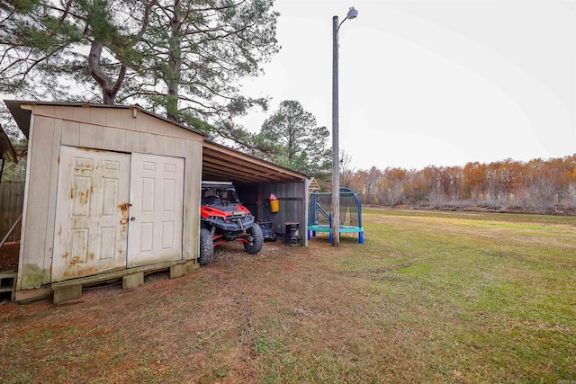 view of outbuilding with a trampoline, a carport, and a lawn