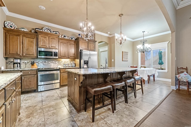 kitchen featuring a kitchen island with sink, a kitchen breakfast bar, sink, ornamental molding, and stainless steel appliances