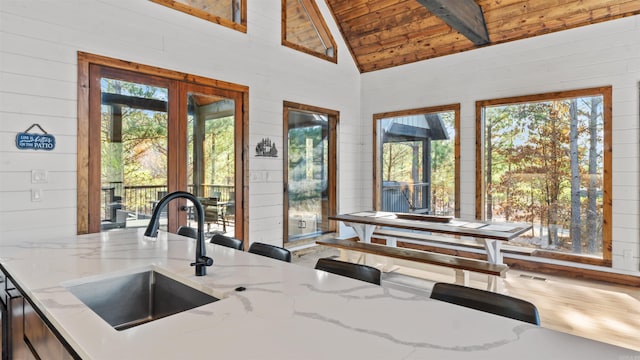 kitchen with wood walls, sink, vaulted ceiling with beams, light stone countertops, and wood ceiling