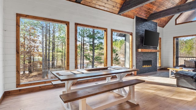 dining room with vaulted ceiling with beams, plenty of natural light, a stone fireplace, and light hardwood / wood-style flooring