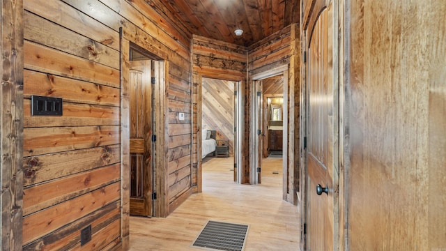 corridor with wooden walls, light hardwood / wood-style flooring, and wood ceiling