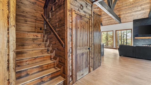 staircase with a fireplace, wood-type flooring, high vaulted ceiling, beamed ceiling, and wood walls