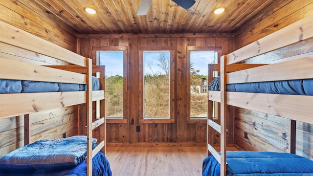 bedroom with multiple windows, wood walls, wooden ceiling, and light wood-type flooring