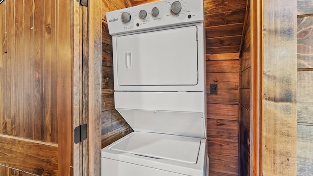 clothes washing area with stacked washing maching and dryer and wooden walls