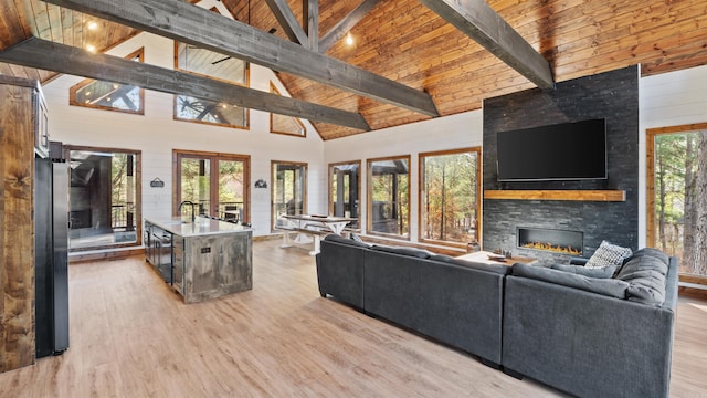 living room featuring beamed ceiling, high vaulted ceiling, a stone fireplace, and plenty of natural light