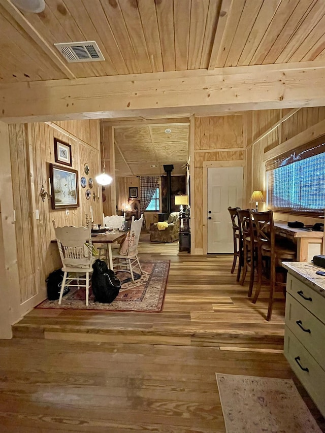 dining area with beamed ceiling, light hardwood / wood-style floors, wooden ceiling, and wood walls