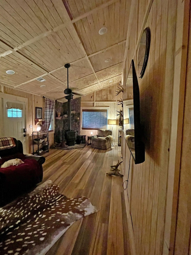 living room featuring wood ceiling, wooden walls, hardwood / wood-style floors, a wood stove, and lofted ceiling