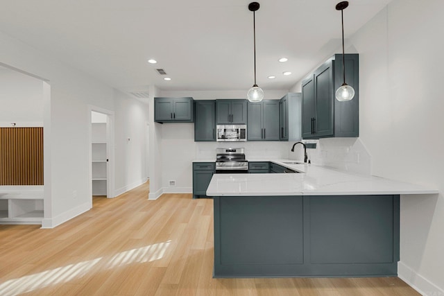 kitchen with kitchen peninsula, appliances with stainless steel finishes, light wood-type flooring, sink, and hanging light fixtures