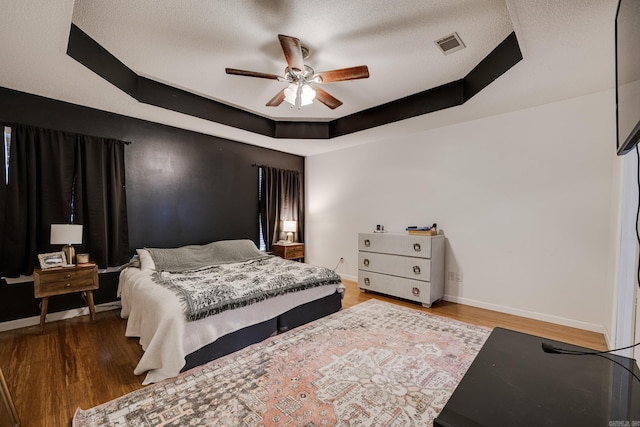 bedroom featuring hardwood / wood-style floors, a textured ceiling, a tray ceiling, and ceiling fan