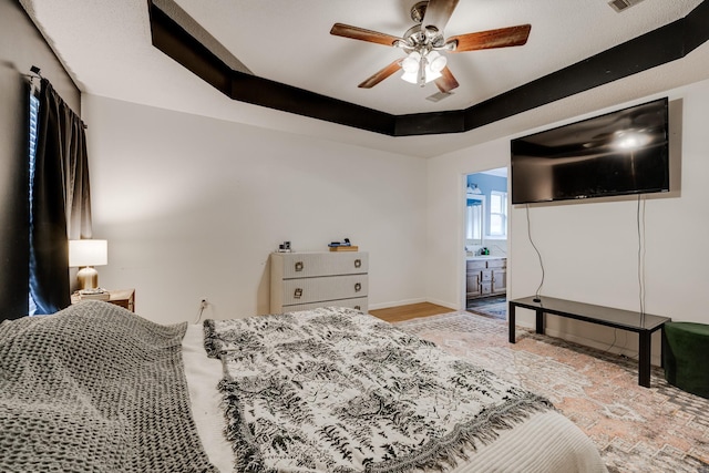 bedroom featuring a raised ceiling, connected bathroom, light hardwood / wood-style flooring, and ceiling fan