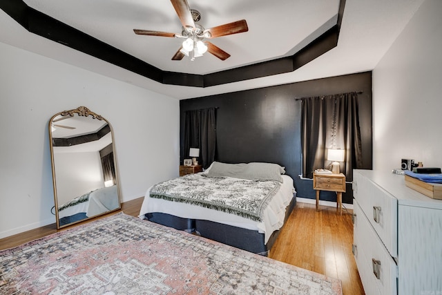 bedroom featuring light wood-type flooring, a tray ceiling, and ceiling fan