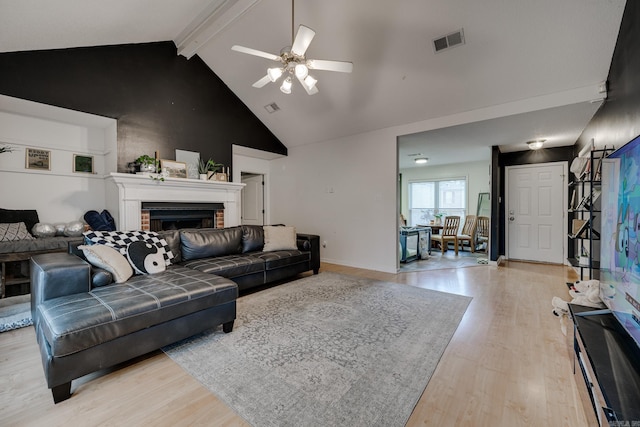 living room featuring lofted ceiling with beams, ceiling fan, light wood-type flooring, and a brick fireplace