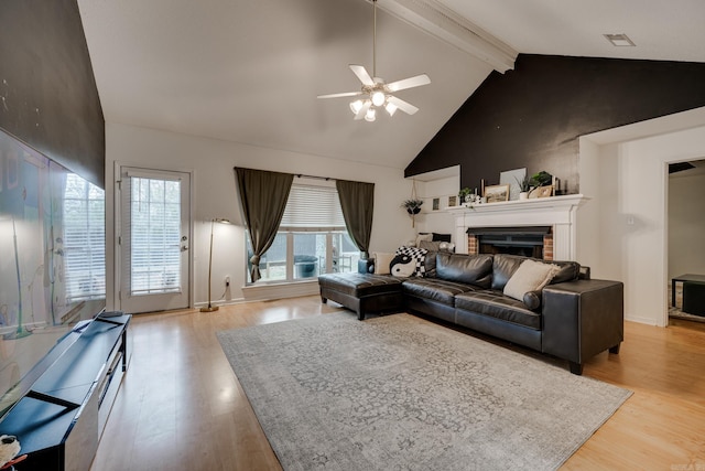 living room with a brick fireplace, ceiling fan, beam ceiling, high vaulted ceiling, and light hardwood / wood-style flooring