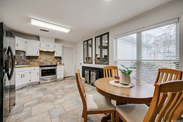 kitchen featuring decorative backsplash, black refrigerator, stainless steel range, crown molding, and white cabinetry