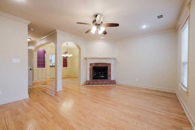 unfurnished living room featuring a brick fireplace, light hardwood / wood-style floors, ceiling fan with notable chandelier, and ornamental molding