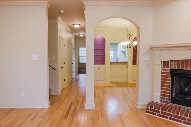 unfurnished living room with crown molding, a fireplace, light hardwood / wood-style floors, and an inviting chandelier