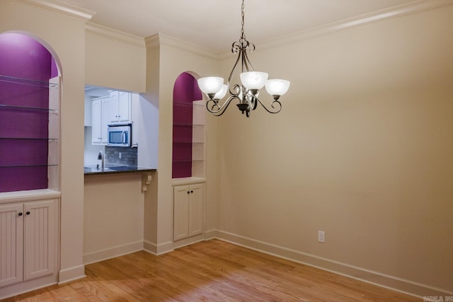 unfurnished dining area featuring crown molding, sink, light hardwood / wood-style floors, and an inviting chandelier