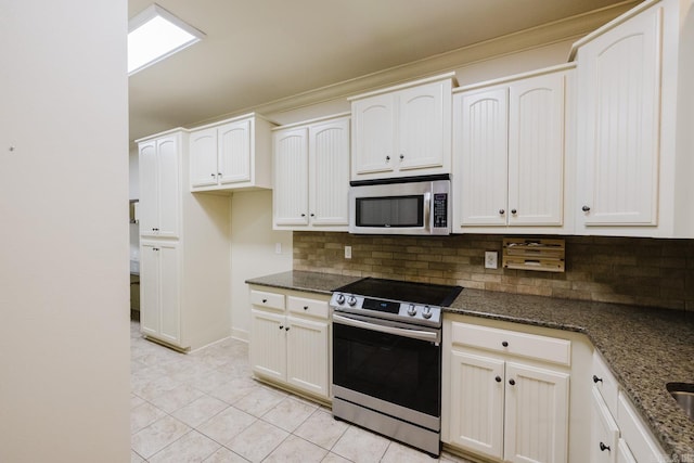 kitchen featuring decorative backsplash, stainless steel appliances, dark stone countertops, white cabinets, and light tile patterned flooring