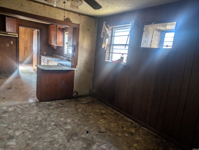 kitchen with ceiling fan, wood walls, kitchen peninsula, sink, and a textured ceiling