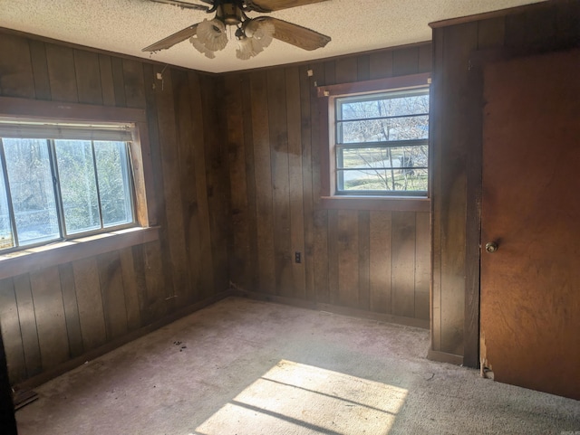 carpeted spare room with wood walls, ceiling fan, and plenty of natural light