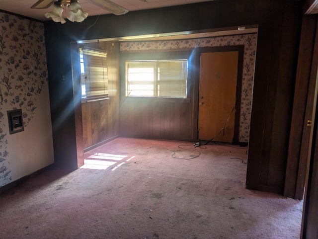 empty room with ceiling fan, light colored carpet, and wood walls