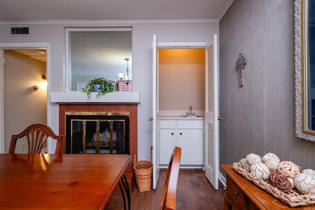 dining area with a textured ceiling, crown molding, dark wood-type flooring, sink, and a fireplace