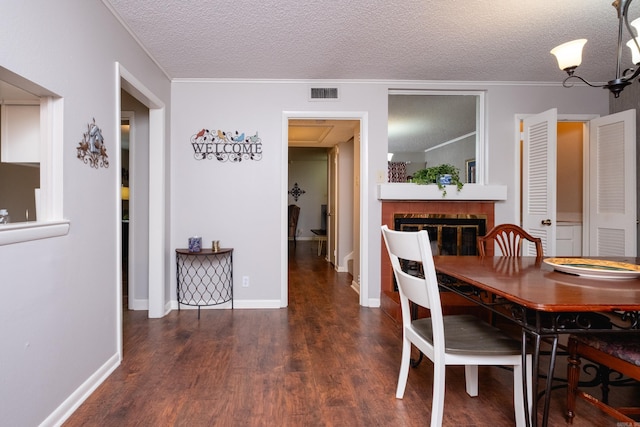 dining area featuring dark wood-type flooring, crown molding, a chandelier, a textured ceiling, and a fireplace